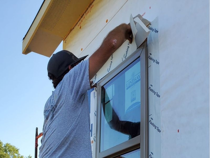 A framer applying high-performance flashing tape around an exterior window