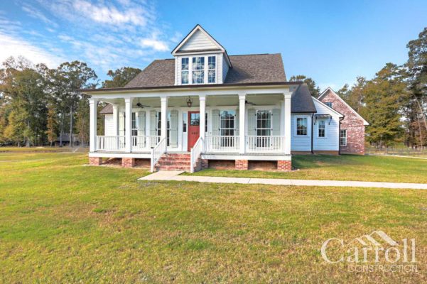 Angled front view of Acadian farmhouse showing red door, dormer, and attached garage