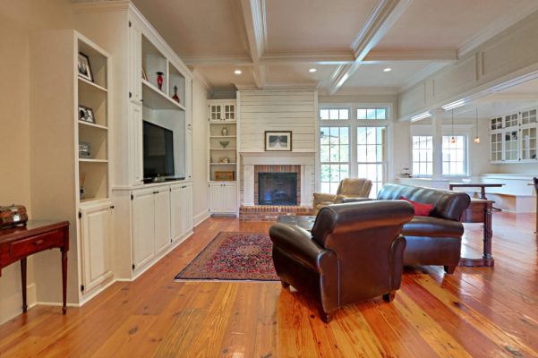 Customized Liberty Plan – Living room with fireplace, built-in entertainment cabinet, coffered ceiling, and paneled kitchen opening