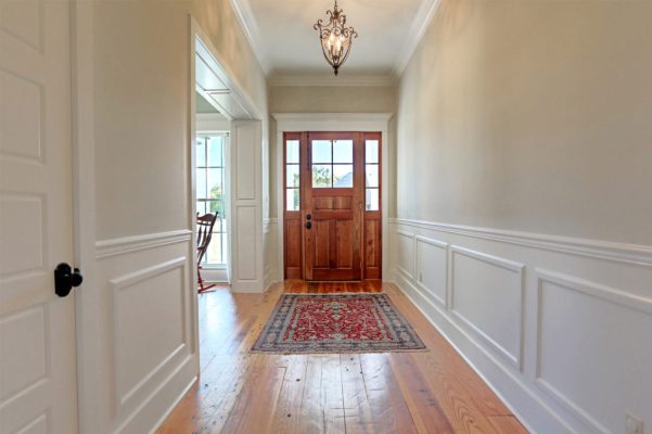 Foyer with stained wood front door, heart pine flooring, chair rail, and paneled cased opening