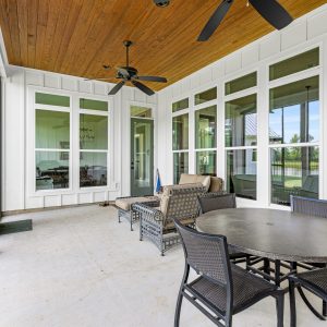 Covered porch with a stained v-groove ceiling, oriented toward a wall of windows that fill the interior with natural light in the Dittmar Liberty home. Dittmar Home – Liberty plan, 2,574 SF – porch with stained wood v-groove ceiling facing wall of windows for natural light.